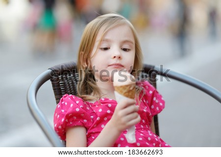 Adorable little girl eating ice-cream outdoors at summer
