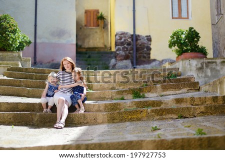 Two cute little sisters and their mother  sitting on stairs in italian town