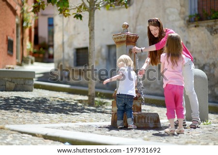 Two sisters and their mother having fun with drinking water fountain in Italy