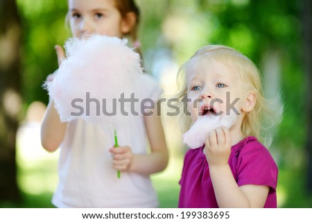 Adorable little sisters eating candy-floss outdoors at summer