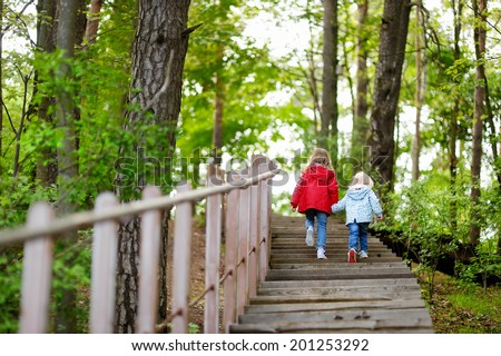 Two little sisters walking up stairs in summer park on beautiful sunny day
