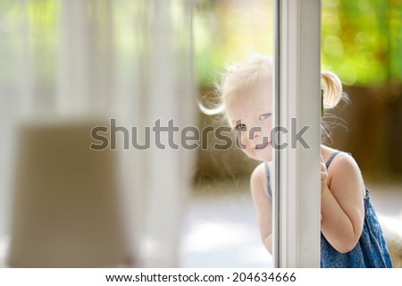 Cute little toddler girl peeking into a window on beautiful warm and sunny summer day