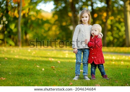 Two little sisters hugging each other in beautiful autumn park on a sunny day
