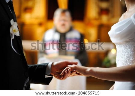 Bride and groom are holding each other\'s hands during church wedding ceremony