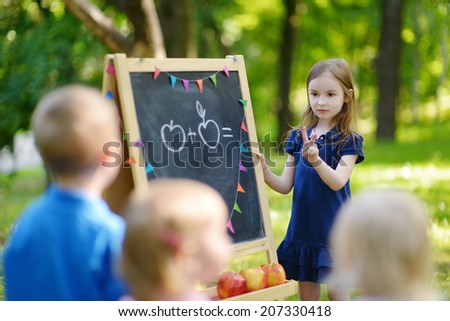 Adorable little girl playing a teacher standing by a blackboard in front of her little students