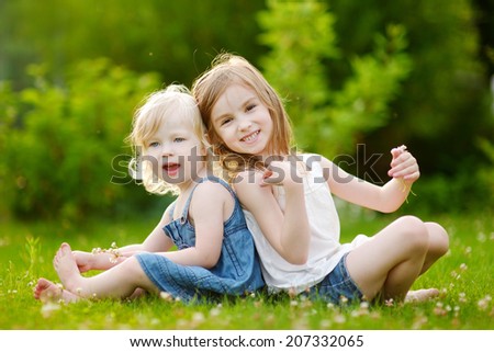 Two cute little sisters having fun while sitting on the grass on a sunny summer day