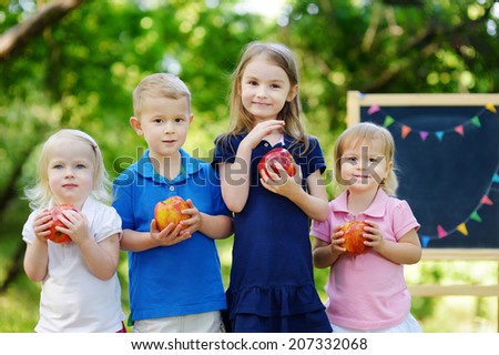 Four adorable little kids holding healthy organic apples in summer park on beautiful sunny day