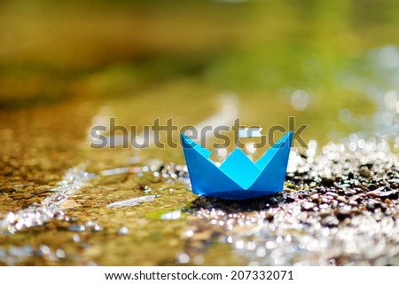 Blue paper boat with a white flag floating on a river
