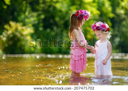 Two adorable little sisters wearing flower crowns by a river on warm and sunny summer day
