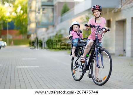 Young mother and her cute little toddler daughter in a child seat getting ready to ride a bicycle
