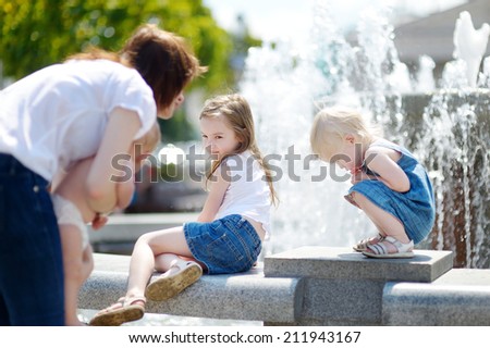 Young woman and three little kids having fun by a city fountain on hot and sunny summer day