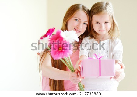 Young mother and her little daughter giving a gift wrapped in pink wrapping paper and flowers