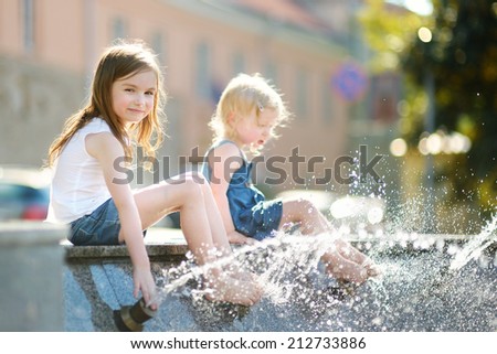 Two cute little girls playing with a city fountain on hot and sunny summer day