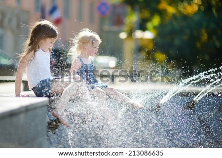 Two cute little girls playing with a city fountain on hot and sunny summer day