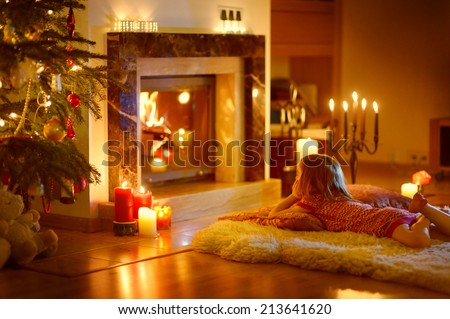 Happy little girl laying by a fireplace in a cozy dark living room on Christmas eve, unfocused