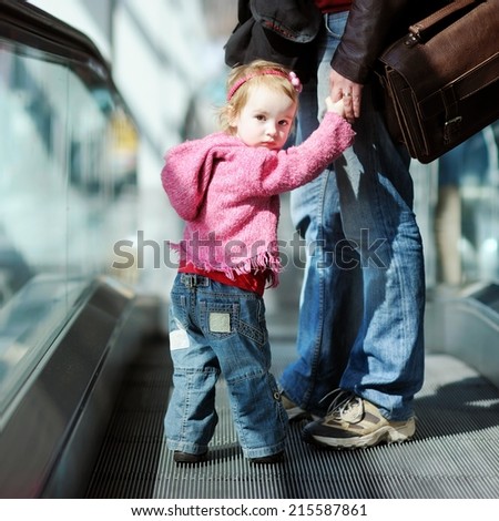 Adorable toddler girl and her father standing on moving escalator
