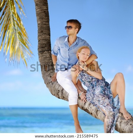 Beautiful young couple sitting on palm tree on a beach