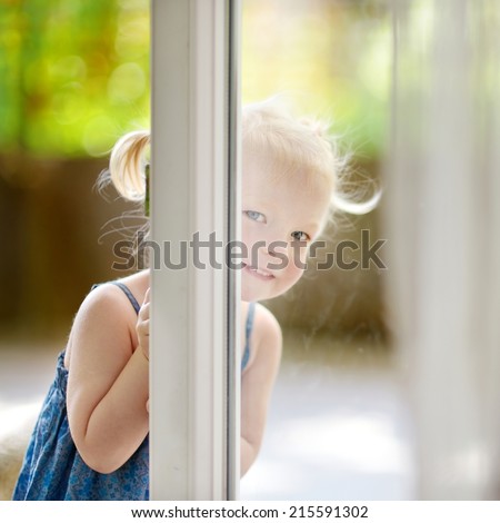 Cute little toddler girl peeking into a window on beautiful warm and sunny summer day