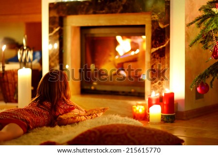 Happy little girl laying by a fireplace in a cozy dark living room on Christmas eve