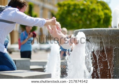 Young father and his baby son having fun by a city fountain on hot and sunny summer day