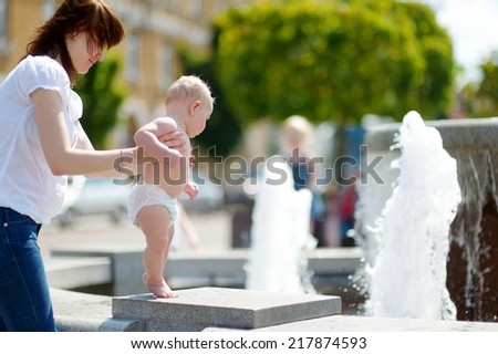 Young mother and her baby son having fun by a city fountain on hot and sunny summer day