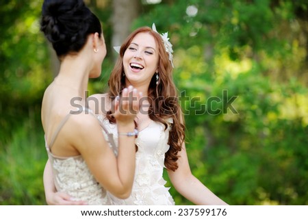 Young bride and her bridesmaid hugging in beautiful summer park