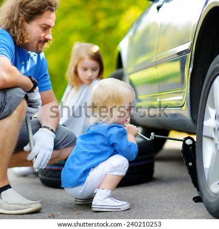 Adorable little girl helping her father to change a car wheel outdoors on beautiful summer day