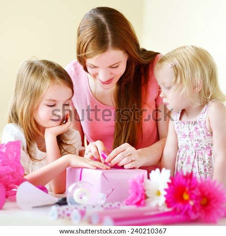 Young mother and her two little daughters wrapping a gift with pink wrapping paper
