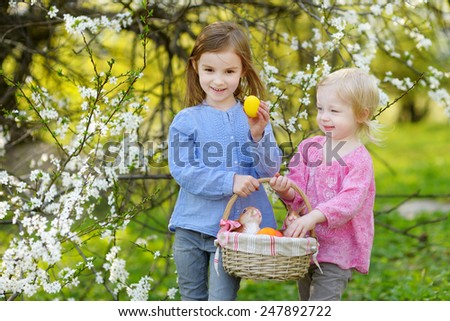 Two little sisters holding a basket of Easter eggs in blooming spring garden on Easter day