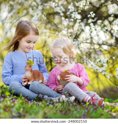 Two adorable little sisters playing with Easter bunnies in blooming spring garden on Easter day