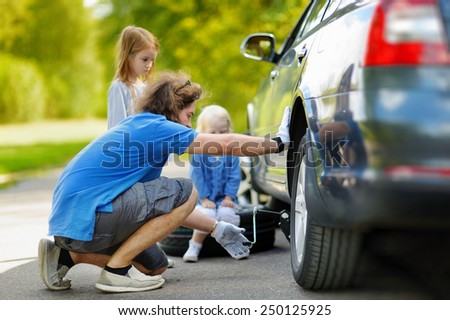 Young father and his two daughters changing a car wheel outdoors on beautiful summer day