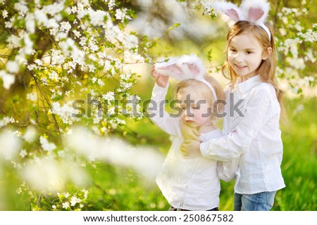 Two adorable little sisters wearing bunny ears in a spring garden on Easter day