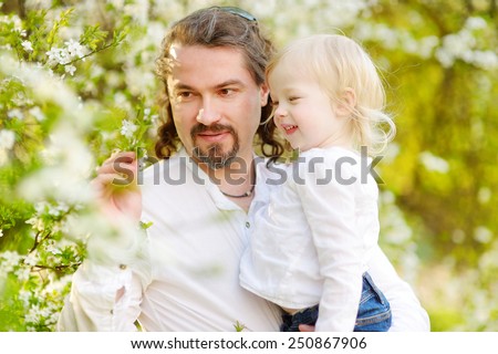 Young father and his adorable toddler daughter having fun in blossoming cherry garden on beautiful spring day