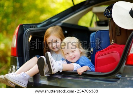 Two adorable little sisters sitting in a car just before leaving for a car vacation with their parents