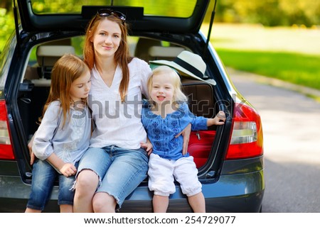 Two adorable little sisters and their mother sitting in a car just before leaving for a car vacation