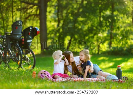 Young mother and her daughters having a picnic in the park on beautiful summer day