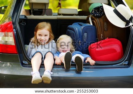 Two adorable little sisters sitting in a car just before leaving for a car vacation with their parents