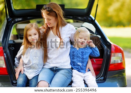 Two adorable little sisters and their mother sitting in a car just before leaving for a car vacation
