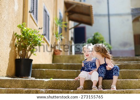 Two cute little sisters sitting on stairs in italian town