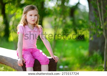 Adorable little girl sitting on a bench in a park on hot and sunny summer day