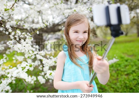 Adorable little girl taking a photo of herself with a selfie stick on beautiful summer day