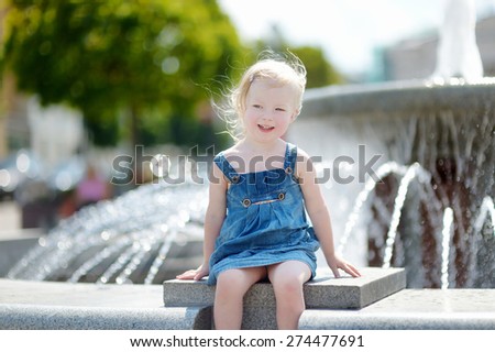 Cute little toddler girl playing with a city fountain on hot and sunny summer day