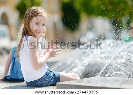 Cute little preschooler girl playing with a city fountain on hot and sunny summer day