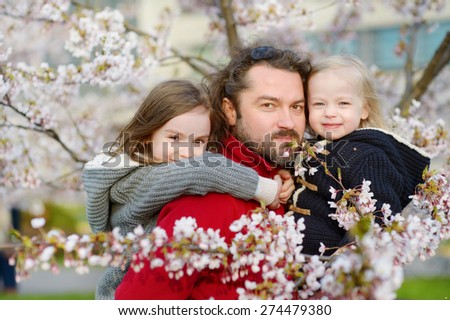 Young father and his children in blooming cherry garden on beautiful spring day