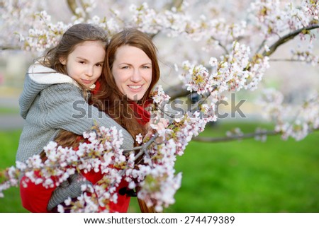 Young mother and her child in blooming cherry garden on beautiful spring day