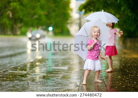 Two cute little sisters standing in a puddle holding umbrella on a rainy summer day