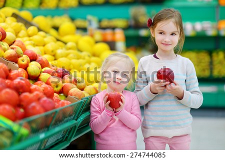 Cute little sisters choosing apples in a food store or a supermarket