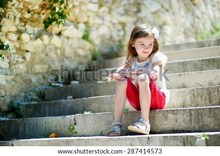 Adorable little girl sitting on stairs on warm and sunny summer day in typical italian town