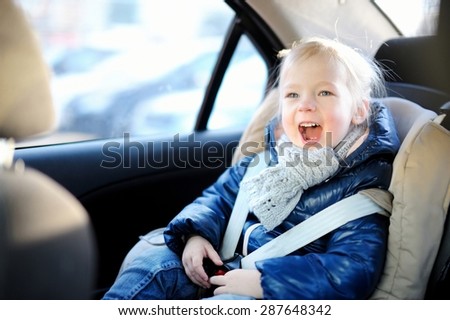 Adorable little girl sitting safely in a car seat