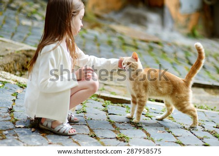Adorable little girl met a cat while walking narrow streets ot typical italian town